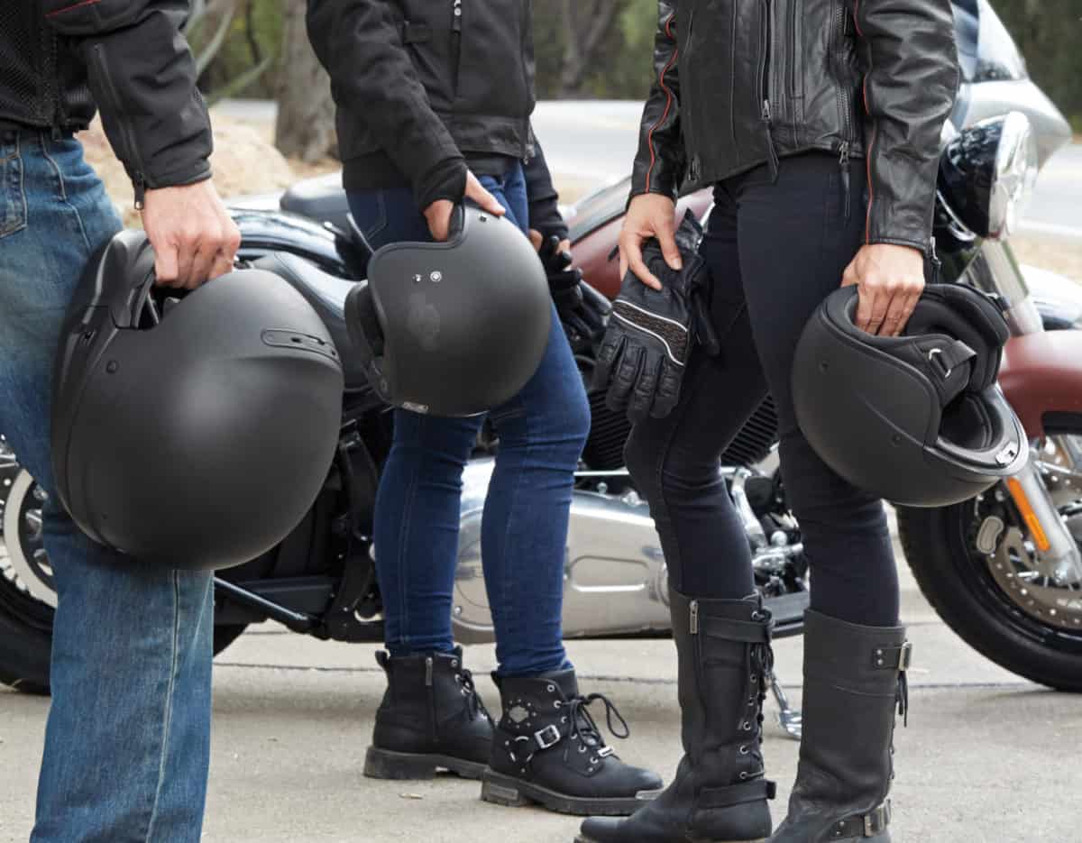 Friends with different types of motorcycle helmets in their hands.
